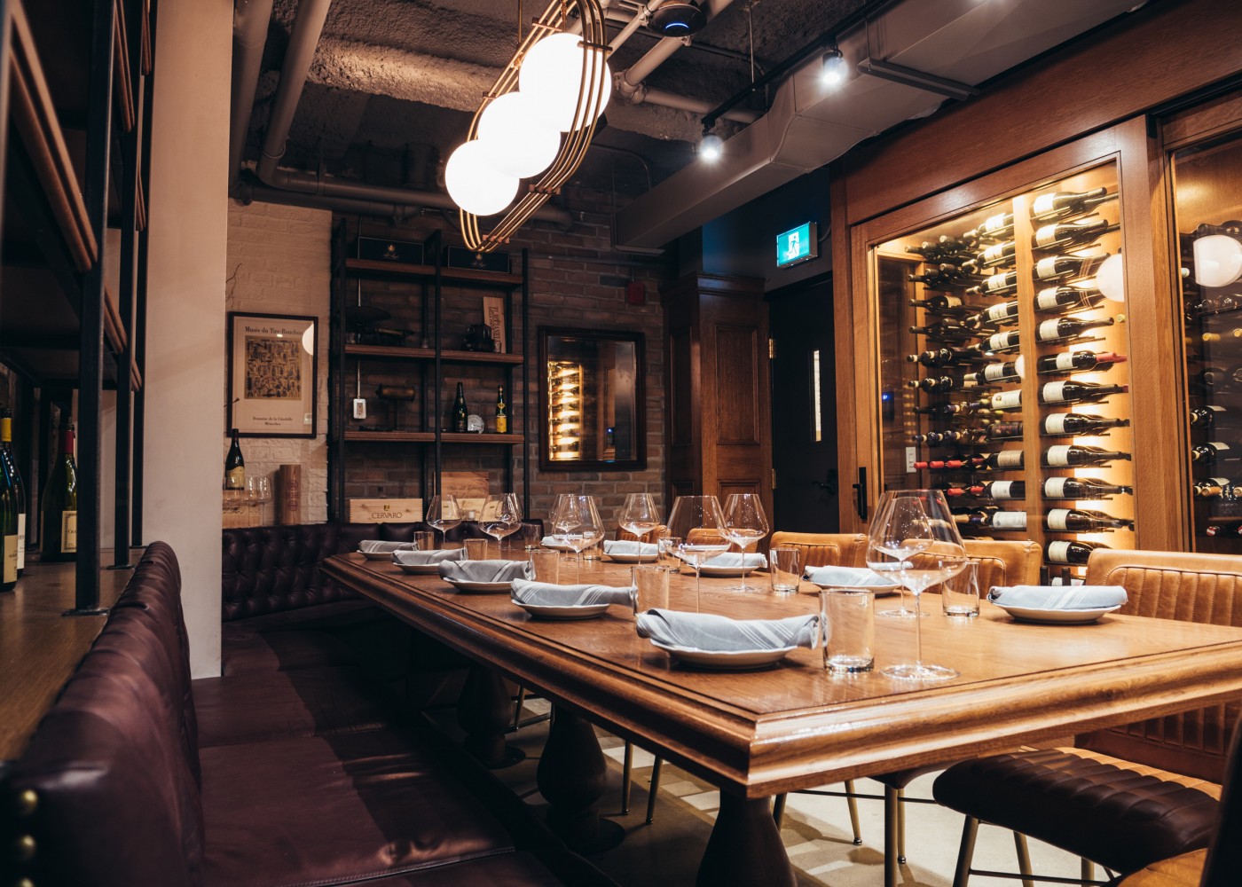 Private dining cellar table with tufted plush seating and shelving with wine bottles.