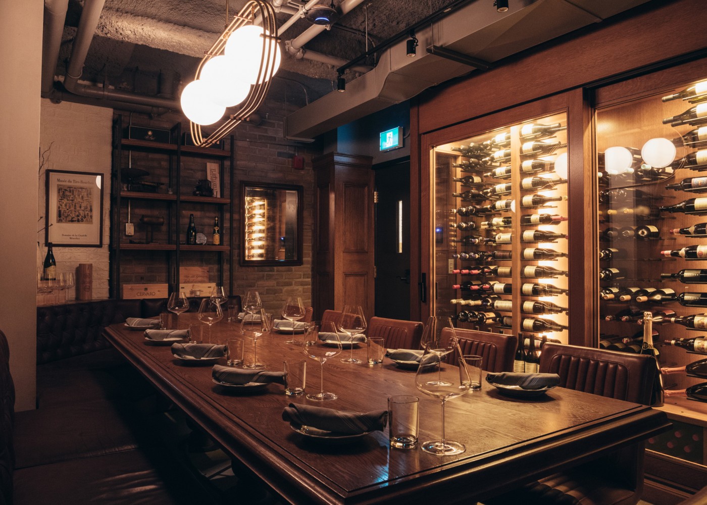 Private dining cellar table with tufted plush seating and shelving with wine bottles.